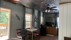 Ein gemütliches Zimmer mit Esstisch, Stühlen, Deckenventilator und einer Küchenzeile inklusive Mikrowelle und Kaffeemaschine.