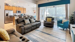 A modern living room with a sofa, armchairs, and a coffee table. There is a kitchen area with cabinets and appliances, and a balcony with a view. - TOP-RATED WINDSOR HILLS Private Home ♥ Pool/Spa, GAME ROOM ♥ 4 mi to DISNEY (Kissimmee)