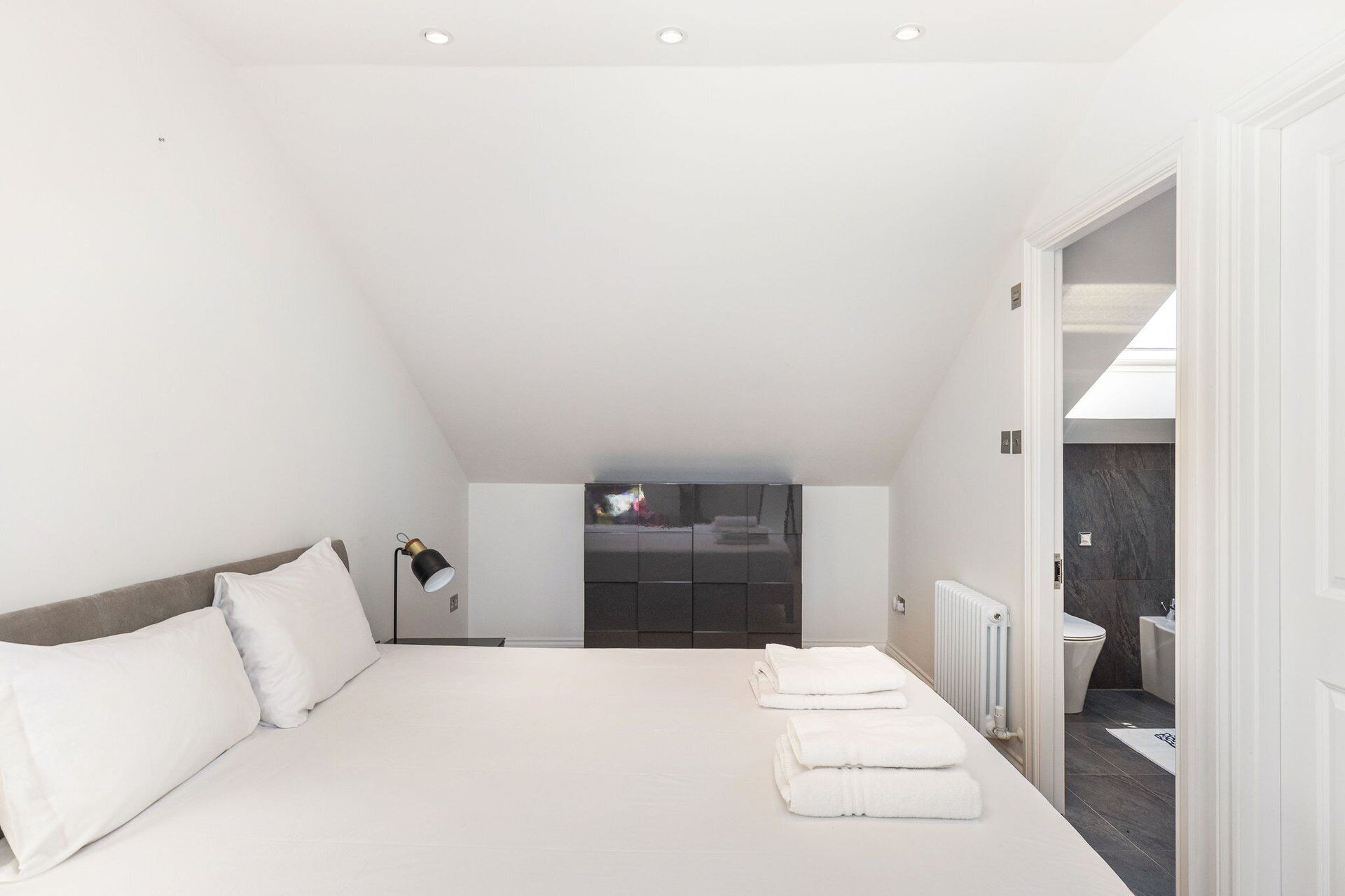 A bedroom with a large bed, a bedside lamp, and a view into the bathroom.
