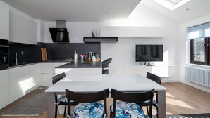 Una cocina moderna con una isla central, una mesa de comedor con sillas, un televisor y una ventana con persianas.