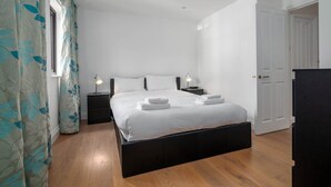 Un dormitorio con una cama grande, dos mesitas de noche, un armario y una puerta.
