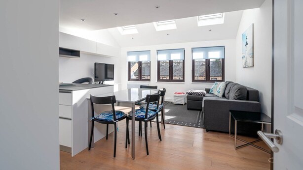 Un apartamento moderno con cocina, comedor y sala de estar. Cuenta con tragaluces, ventanas amplias y un sofá gris.