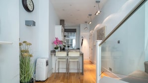 Una cocina estrecha con una isla central, muebles blancos y un moderno colgante de techo.