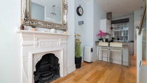 Una habitación con chimenea blanca, un espejo grande, un reloj en la pared y una zona de cocina con barra.