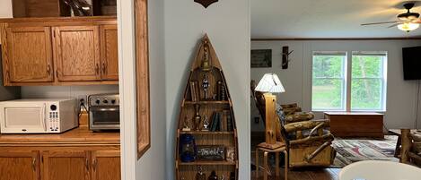 A kitchen with wooden cabinets, a microwave, and a stove. There is a wooden shelf with various items and a wall-mounted clock.