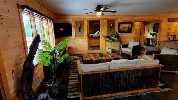 A cozy cabin interior with a wooden interior, a sofa set, a dining table, and a ceiling fan. - Beautiful Home with Lake Views 4/2, Beautiful Home with Lake Views 4/2 - Resort Access for Fee (Lake George)