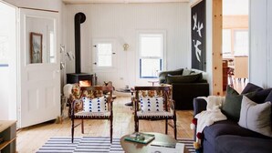 A cozy living room with a fireplace, two floral-patterned chairs, a dark sofa, and a striped rug.