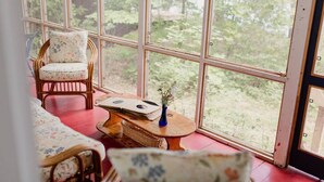 A cozy room with a large window, wicker furniture, and a small table with a vase.