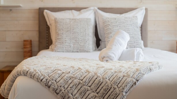 Een net opgemaakt bed met een gebreid plaid en twee kussens.