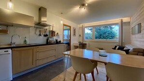 Een moderne keuken met houten kastjes, een inbouwoven en een eethoek met een tafel en stoelen.