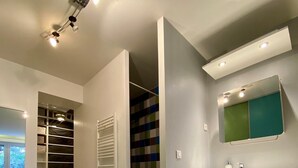 Een moderne badkamer met een grote spiegel, een witte wastafel en een inloopkast met een kleurrijk betegelde achterwand.