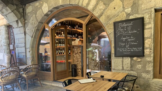 Un café al aire libre con paredes de piedra, mesas y sillas de madera.