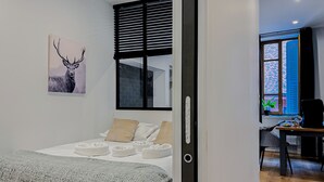 Un dormitorio moderno con una cama, almohadas, una manta, un cuadro colgado en la pared de un ciervo y una ventana con persianas.