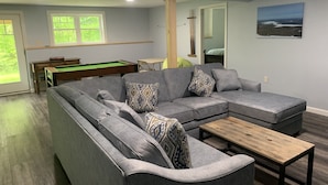 Una sala de estar con un sofá seccional gris, una mesa de billar y una mesa de centro de madera.