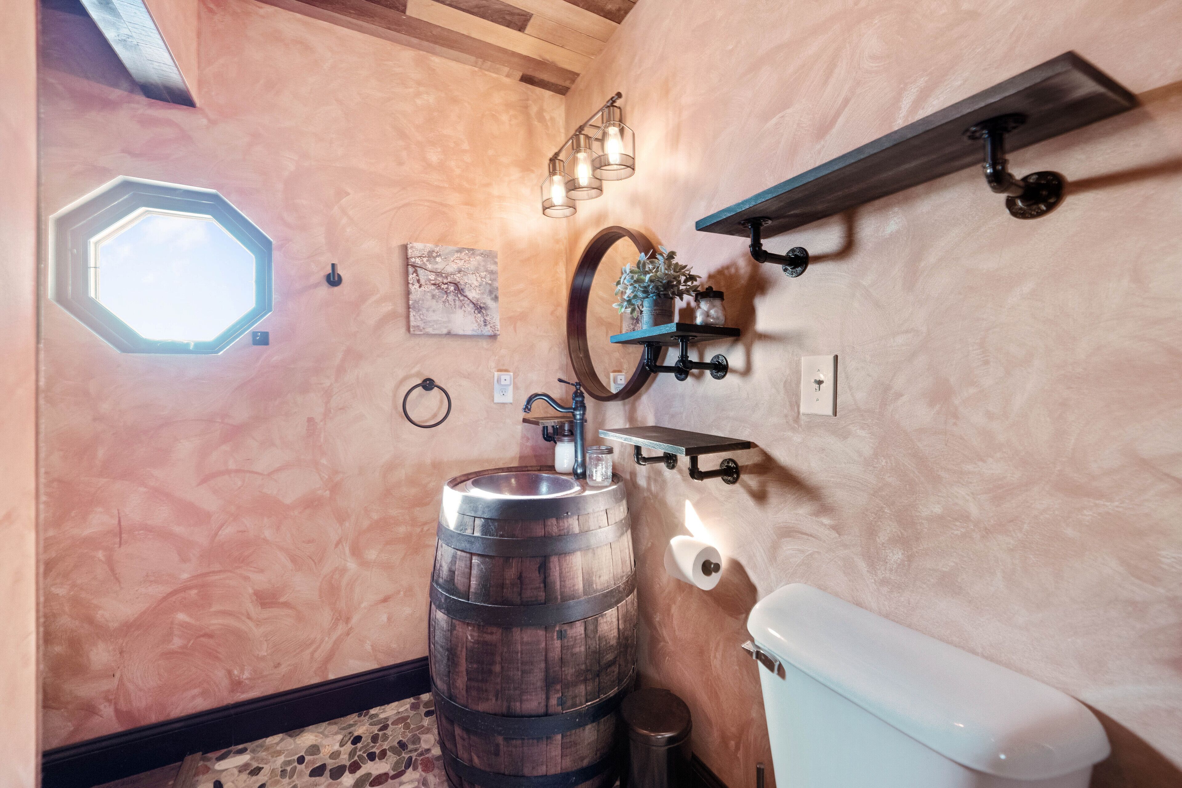 A bathroom with a wooden barrel sink, a white toilet, a mirror, and a skylight.