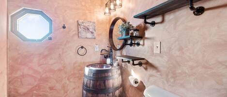 A bathroom with a wooden barrel sink, a white toilet, a mirror, and a skylight.