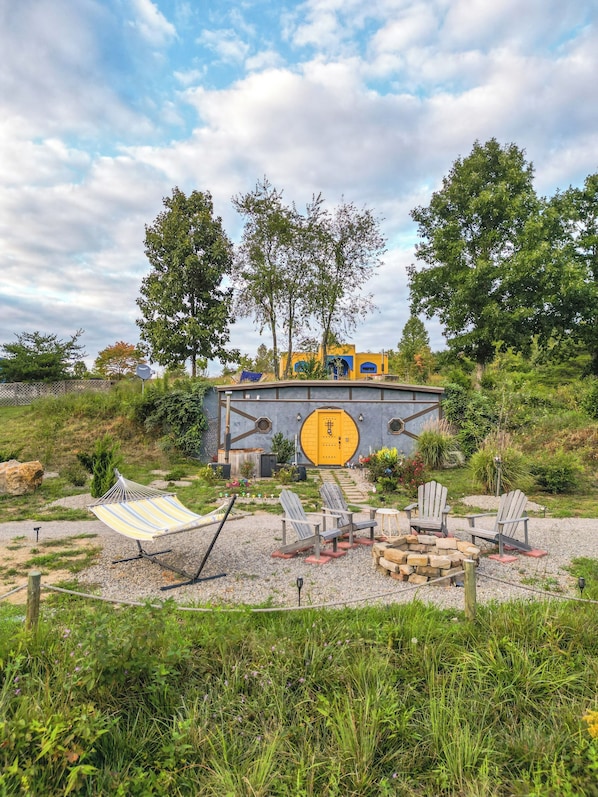 A rustic outdoor seating area with Adirondack chairs, a hammock, and a fire pit.