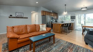 Ein modernes Wohnzimmer mit einer Ledersofa, einem Couchtisch und einer Küchenzeile mit Holzschränken und einem Kühlschrank.