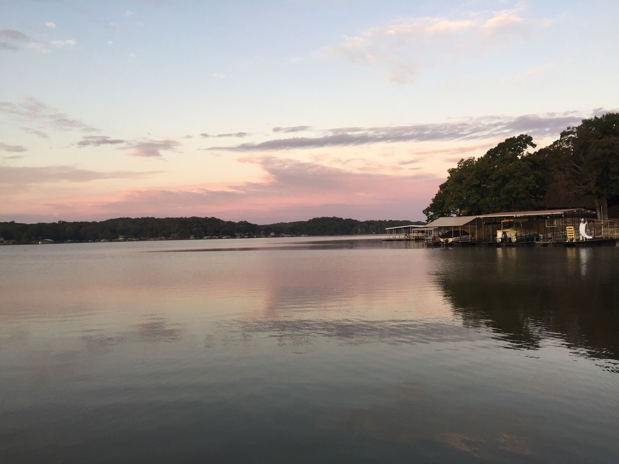 A calm lake with a dock and covered seating area.