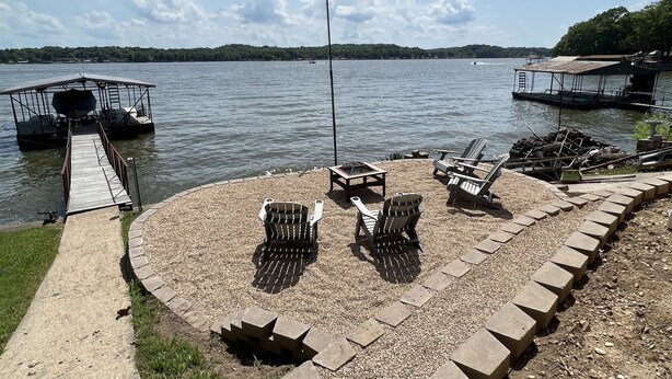 A lakeside deck with Adirondack chairs, a small table, and a dock extending into the water. - Cozy Lake Cabin With Beautiful View! (Gravois Mills)