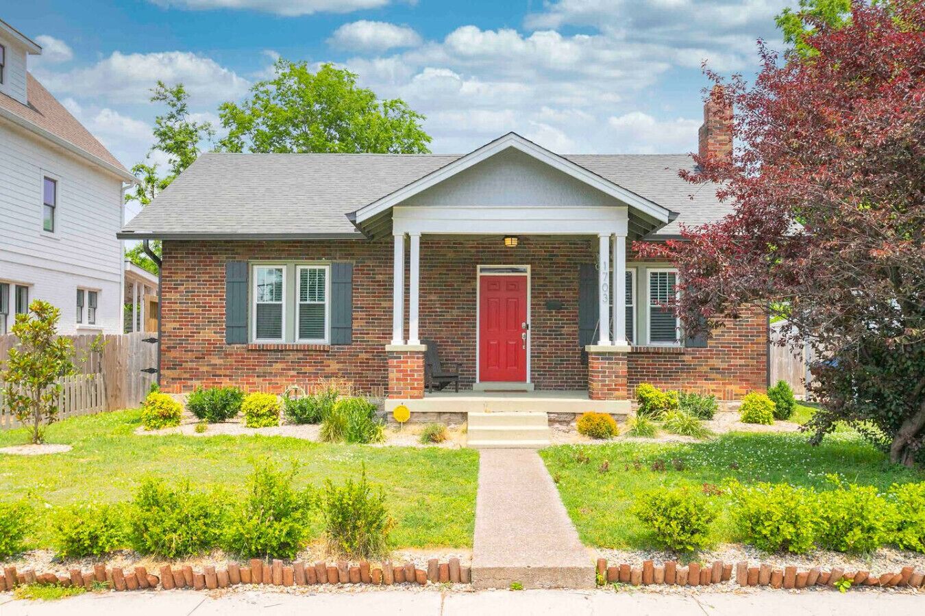 A two-story brick house with a red front door, white columns, and a front porch.