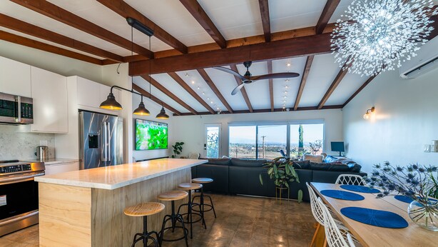Cozinha moderna com ilha central, banquetas de bar e área de jantar com uma mesa comprida e cadeiras.