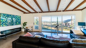 Sala de estar moderna com uma televisão grande, sofá de couro e vista para o exterior através de grandes portas deslizantes.
