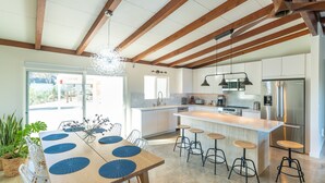 Cozinha moderna com vigas de madeira, uma ilha central com banquetas e uma área de jantar com uma mesa grande e cadeiras.