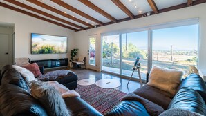 Uma sala de estar ampla com uma grande televisão de tela plana, sofás de couro e vista para o exterior através de amplas janelas.