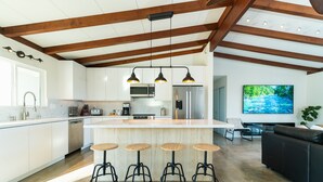Cozinha moderna com ilha central, banquetas de bar e área de jantar com sofá de couro preto.
