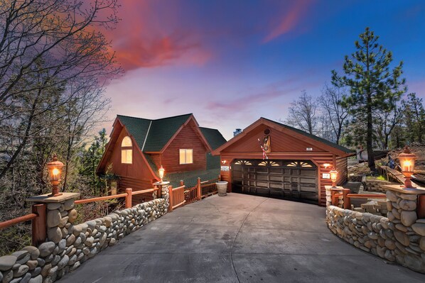 A log cabin with a stone wall entrance, a garage, and a porch with a stone railing.