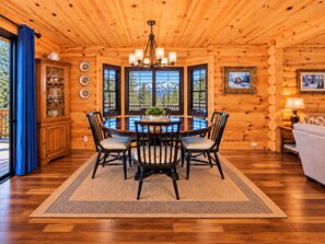 Interior de una cabaña de madera con una mesa de comedor rodeada de sillas, un candelabro y un sofá.