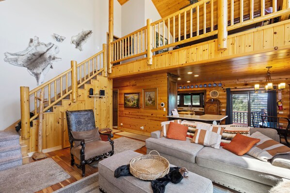 A spacious living area with a wooden staircase, a sofa set, a dining table, and a fireplace.