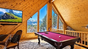 Una stanza in legno con tavolo da biliardo, una poltrona comoda e una televisione che mostra un paesaggio montano.
