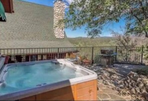 A hot tub in a backyard with a stone wall and a wooden deck.