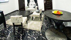 A modern dining area with a marble floor, a round table with a fruit bowl, and a sofa with a patterned throw. - Exquisite 1-bedroom Condo (Lagos)