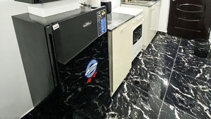 A compact kitchen with a black refrigerator, microwave, and oven. There is a white countertop with a sink and a black tiled floor. - Exquisite 1-bedroom Condo (Lagos)