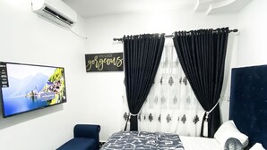 A bedroom with a bed, a TV, a sofa, and curtains. - Exquisite 1-bedroom Condo (Lagos)