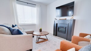 Una sala de estar moderna con un sofá color beige, un sillón naranja, una mesita redonda y una chimenea.