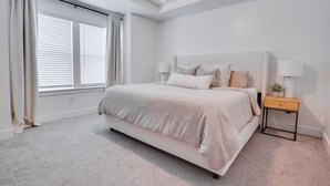 Un dormitorio con cama, mesitas de noche y una ventana con cortinas.