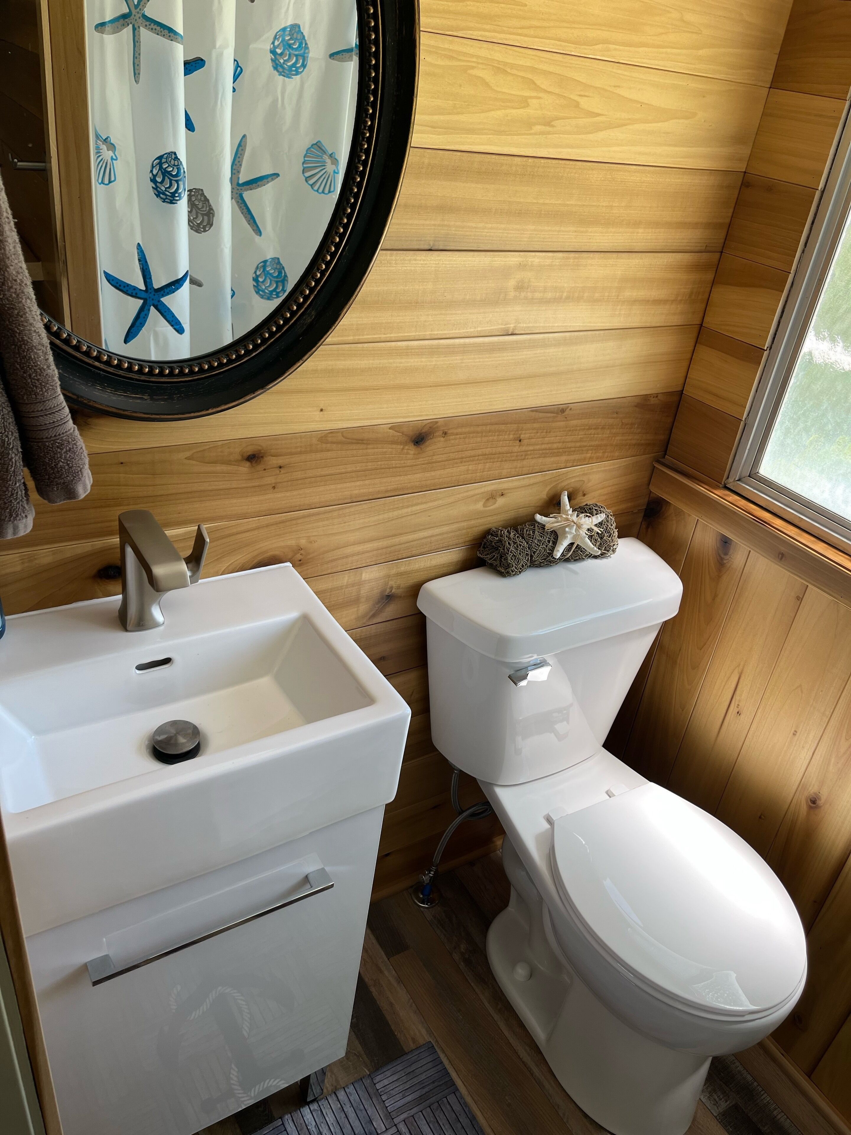 Un baño con paneles de madera, un lavabo blanco, un inodoro y un espejo con motivos de estrellas de mar.