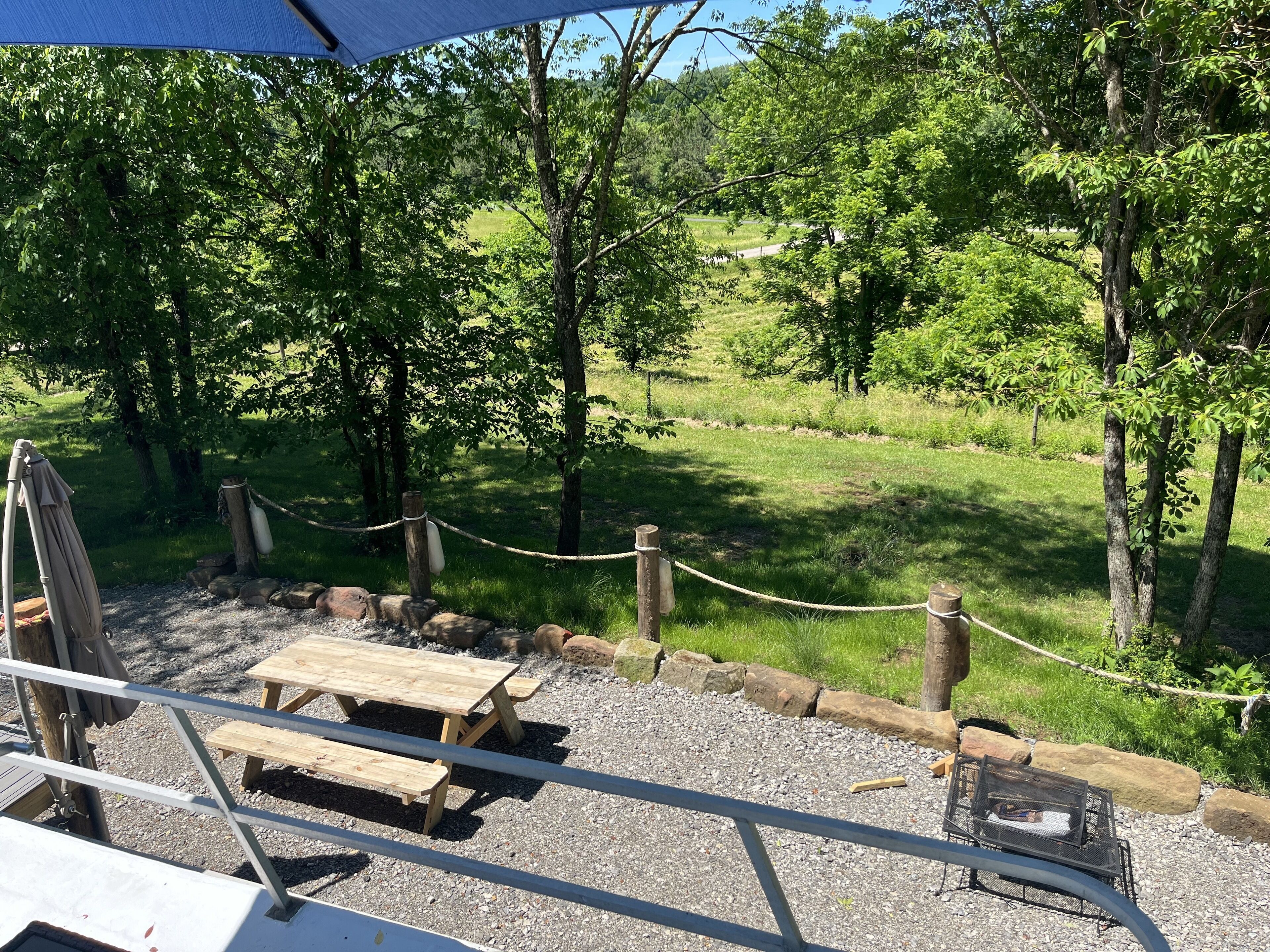 A picnic area with wooden benches and a table, surrounded by a rope barrier and trees.