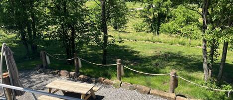 A picnic area with wooden benches and a table, surrounded by a rope barrier and trees.