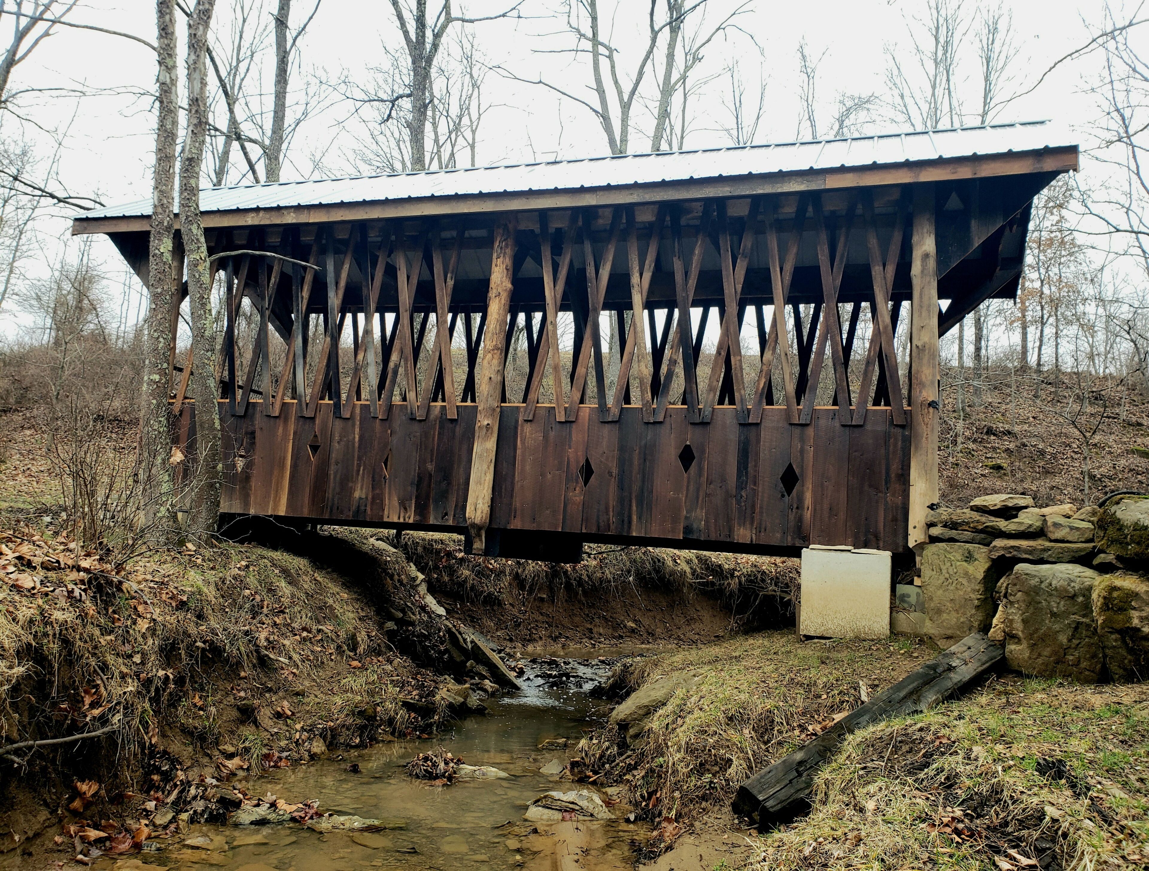 Un ponte di legno rustico che scavalca un piccolo ruscello, circondato da alberi e rocce.