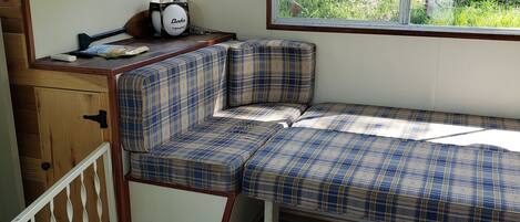 A cozy RV interior with a plaid bench, a small kitchenette, and a window offering a view of greenery.