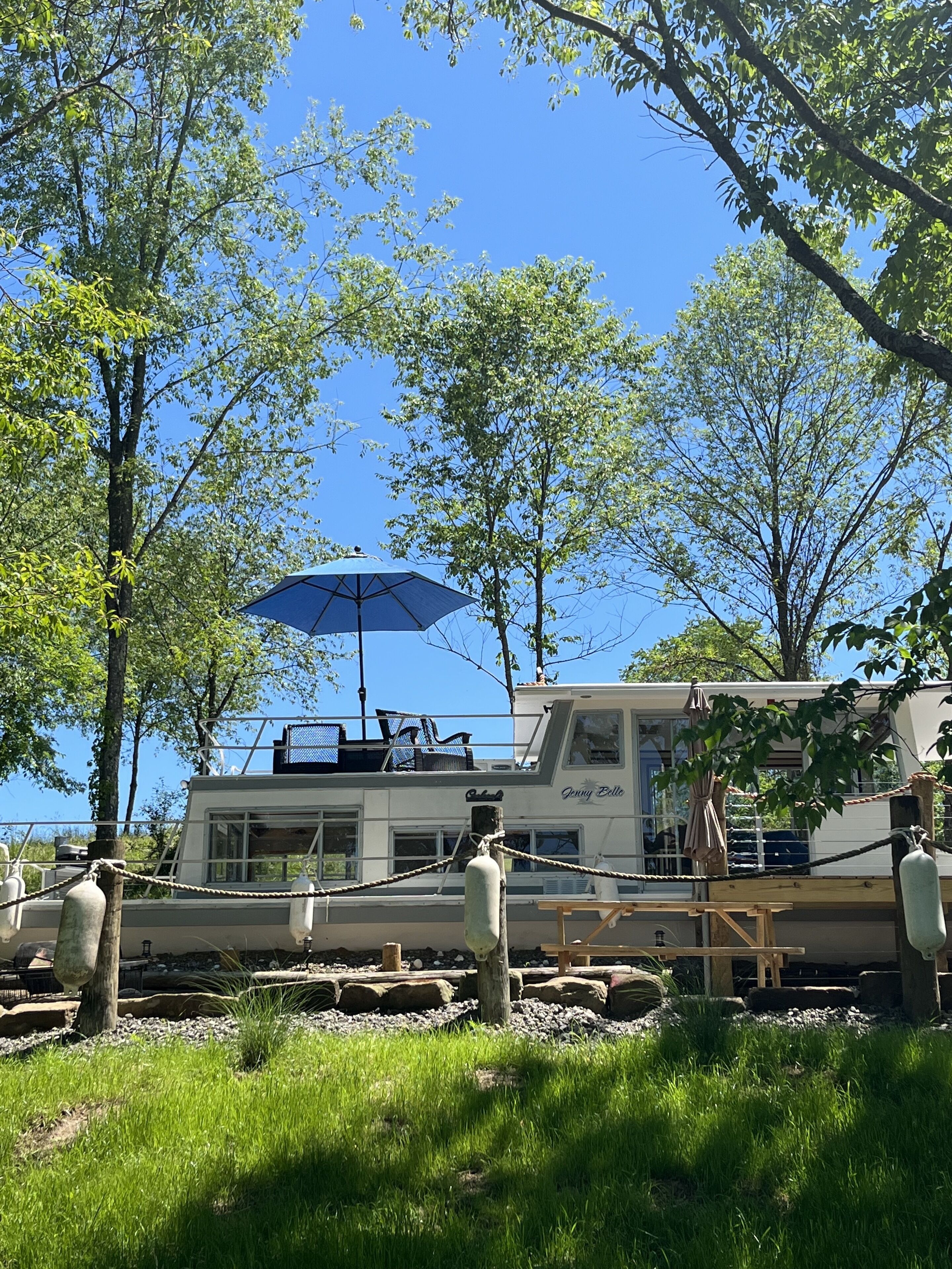 A boat with a blue umbrella, surrounded by trees and a grassy area.