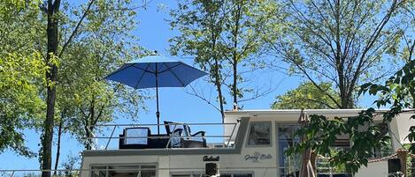 A boat with a blue umbrella, surrounded by trees and a grassy area.