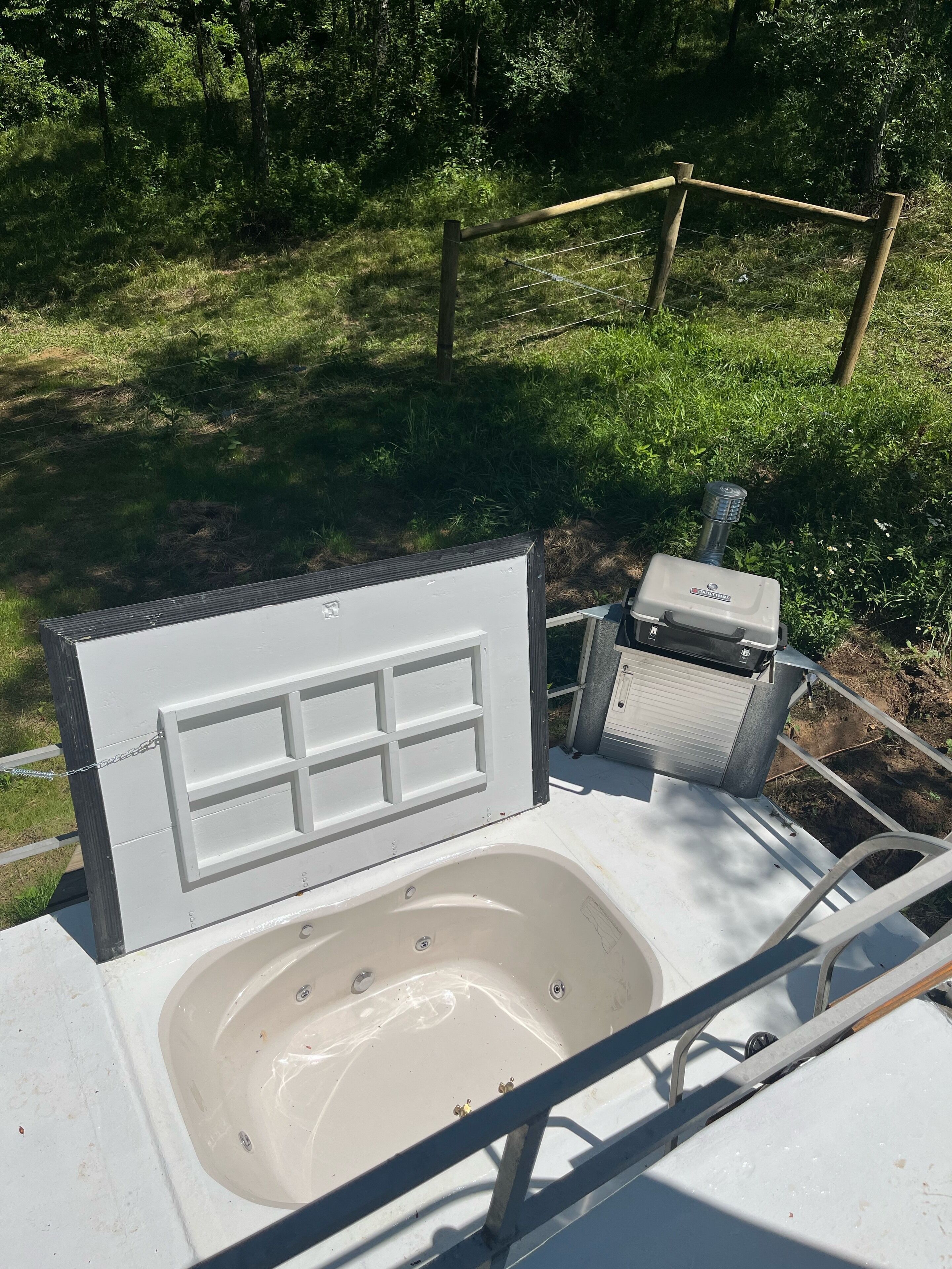 A portable hot tub with a control panel and a water pump, set up outdoors with a wooden fence and greenery in the background.