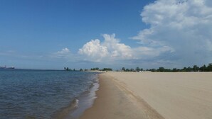 Una playa extensa de arena clara, con olas suaves, cielo despejado y un barco a lo lejos.