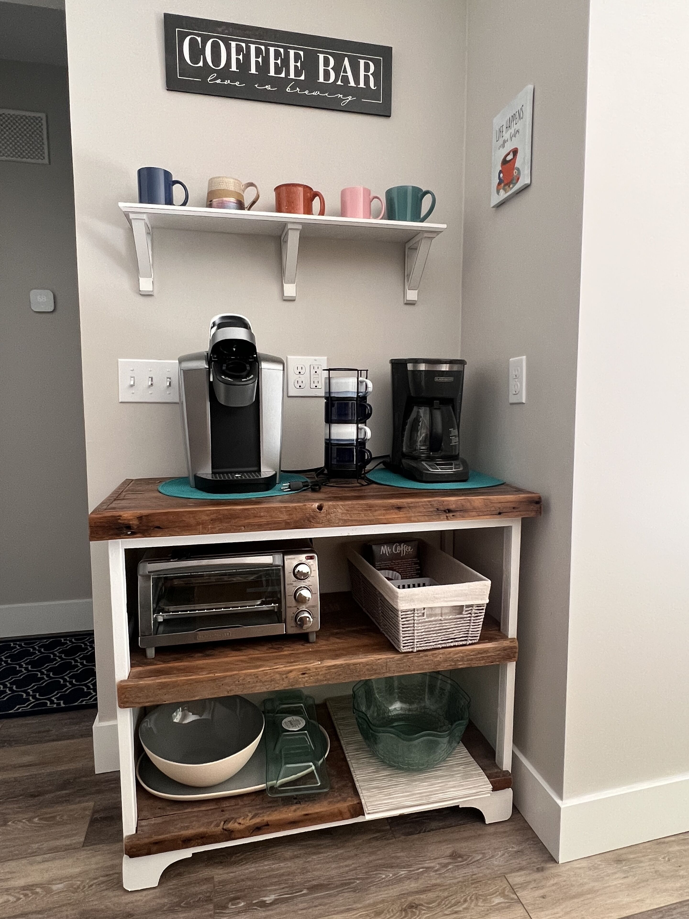 A kitchen area with a coffee bar setup, including a coffee maker, a toaster, and a shelf with mugs.